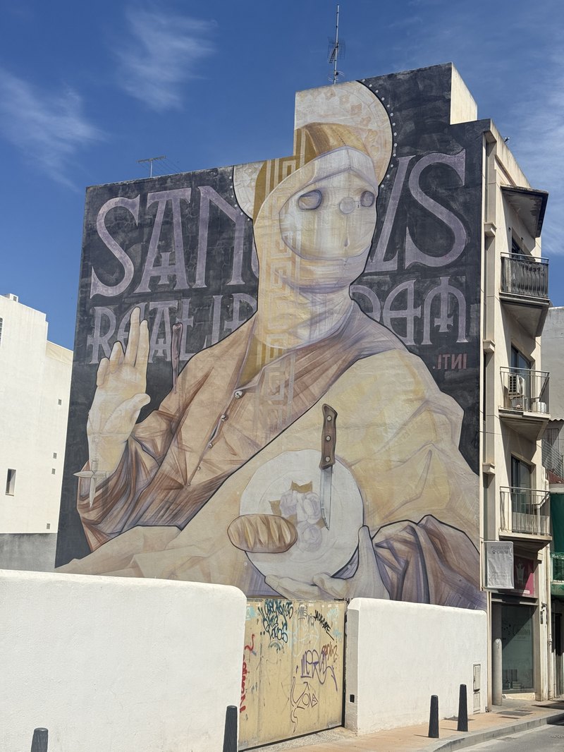 イビサの建物の壁一面に描かれた・パンとナイフを持つ聖人を描いた巨大なストリートアートの壁画