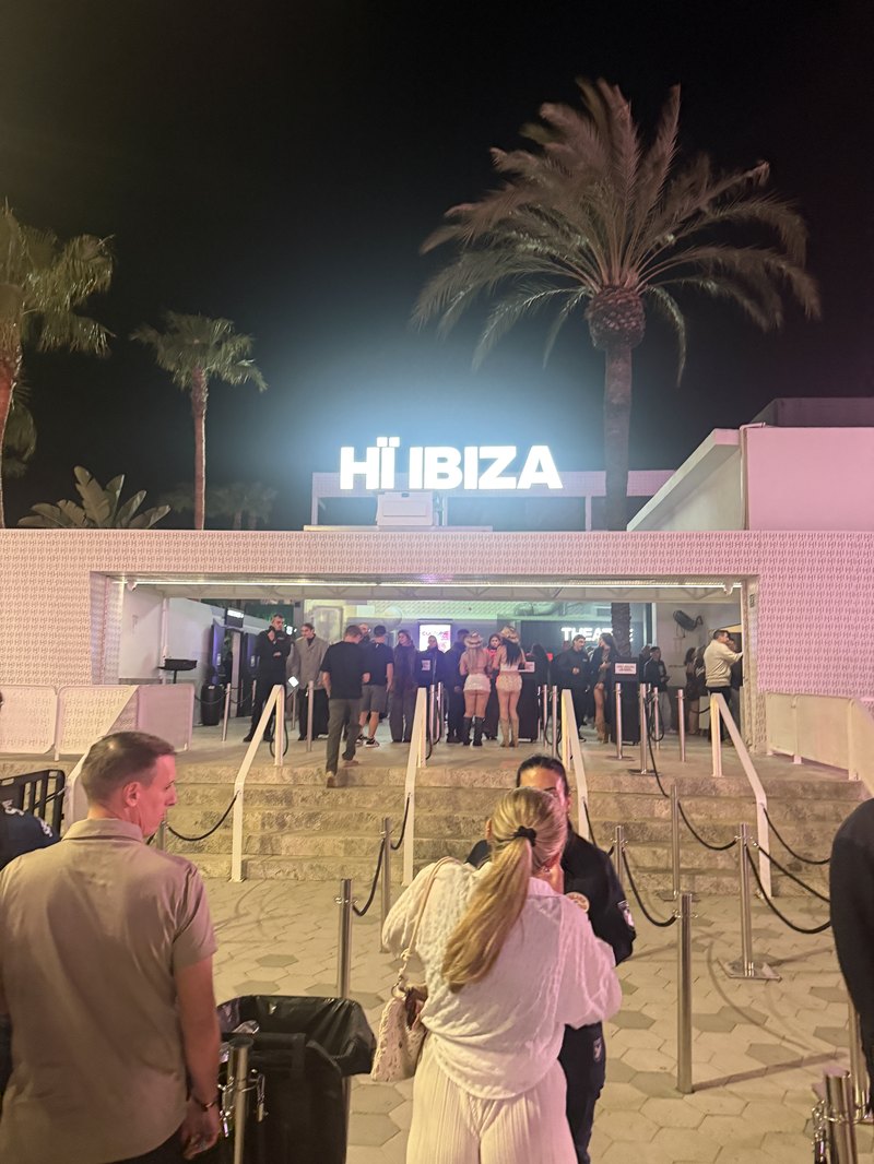 Hï Ibizaの白く光る入口サインとヤシの木・深夜に集まる人々