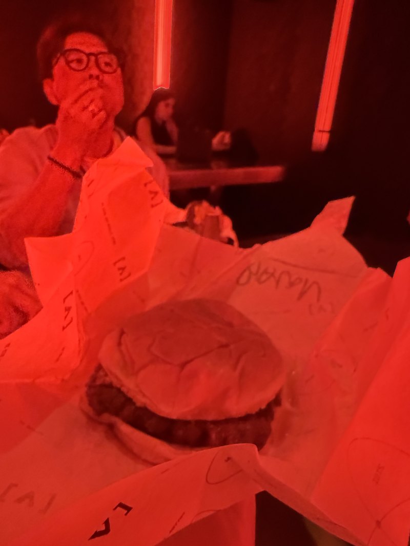深夜のクラブの片隅で頬張る紙包みのハンバーガー・赤い照明