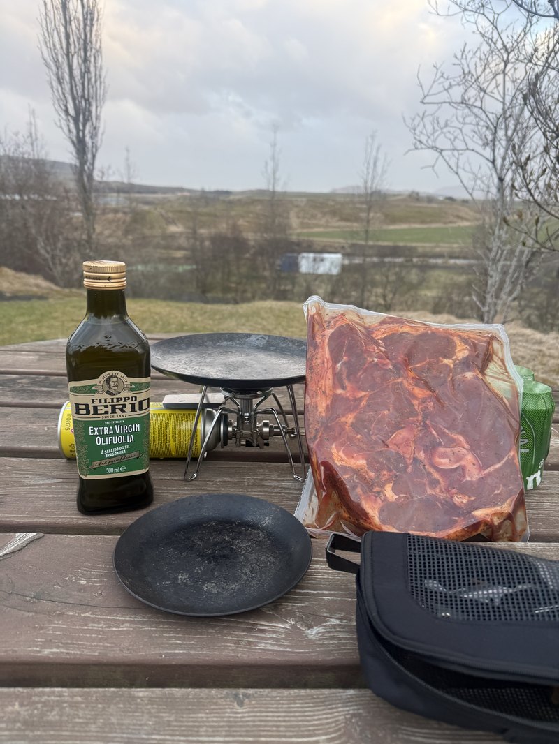 荒野を望むテーブルで、携帯コンロとオリーブオイル・生のラム肉を広げたキャンプ飯の準備