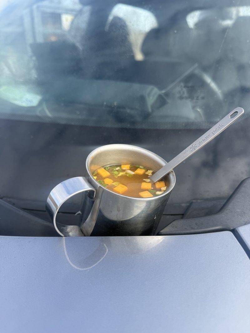 車のボンネットに置かれた、湯気の立つスープのカップとスノーピークのスプーン