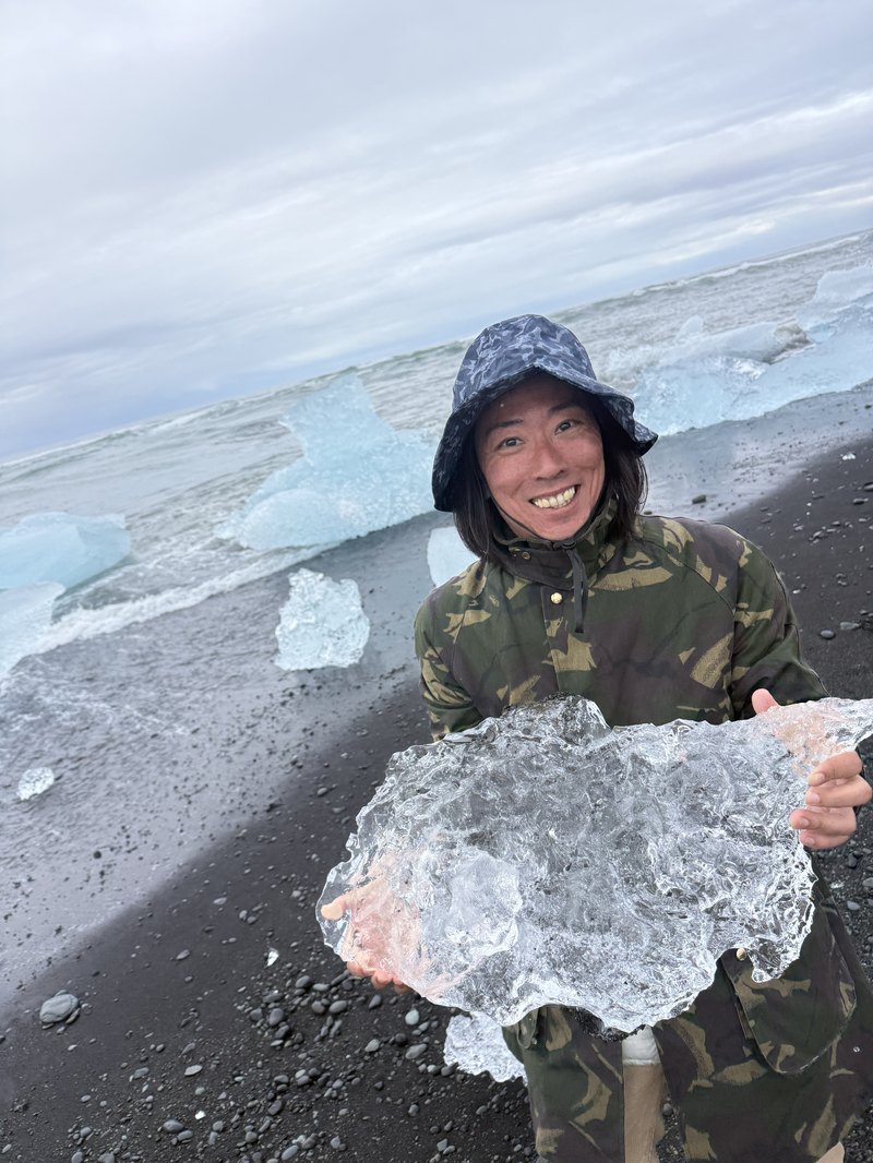 ダイヤモンドビーチの黒い砂浜で透き通った氷河のかけらを抱える筆者の笑顔