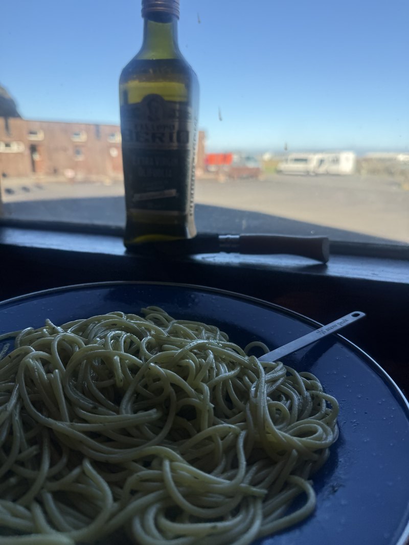 皿に盛られたパスタとオリーブオイル・窓の外にはキャンプ場の景色